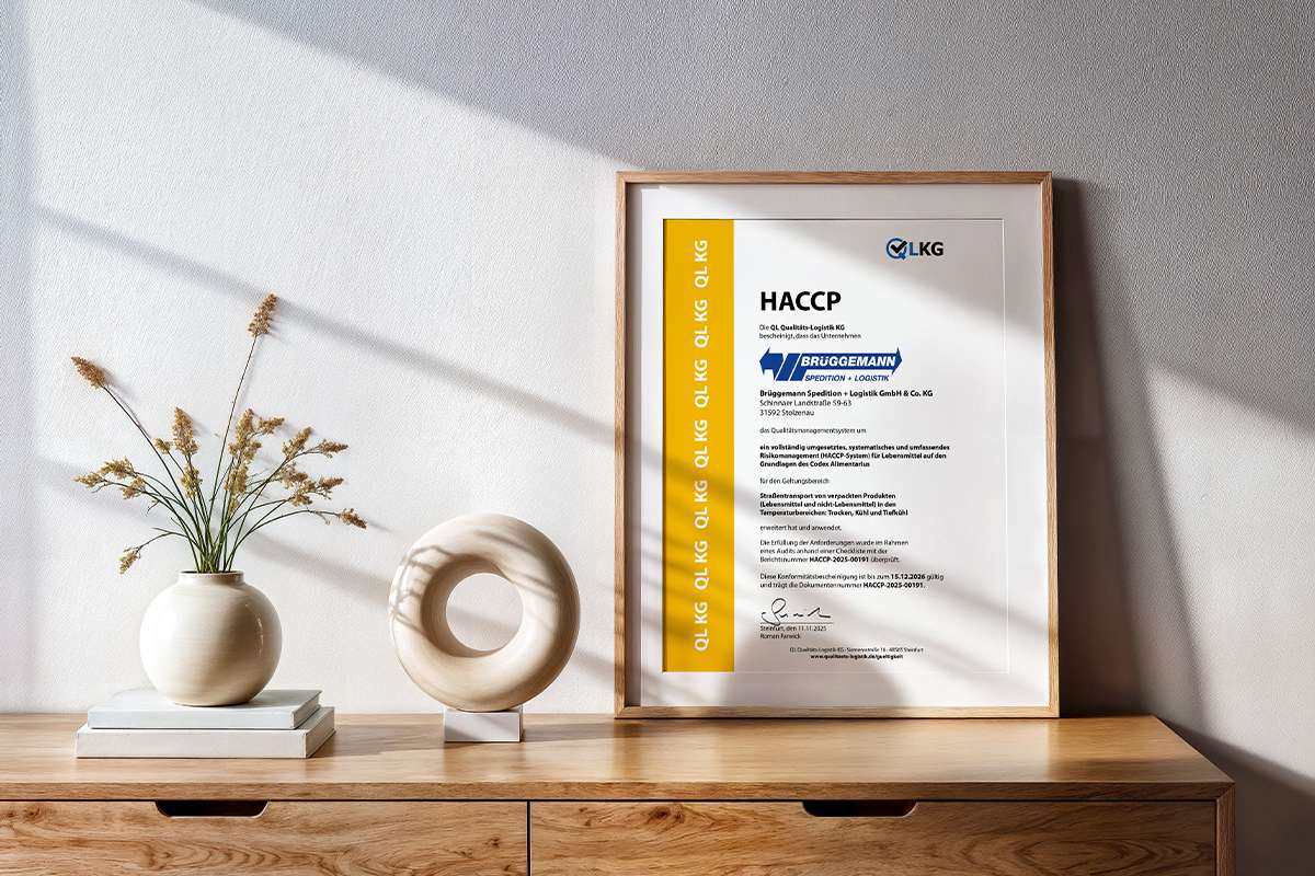 HACCP Zertifikat, ausgestellt an Brüggemann Spedition + Logistik GmbH & Co. KG, in einem Bilderrahmen. Stehend auf einem Sideboard. Daneben Dekoration